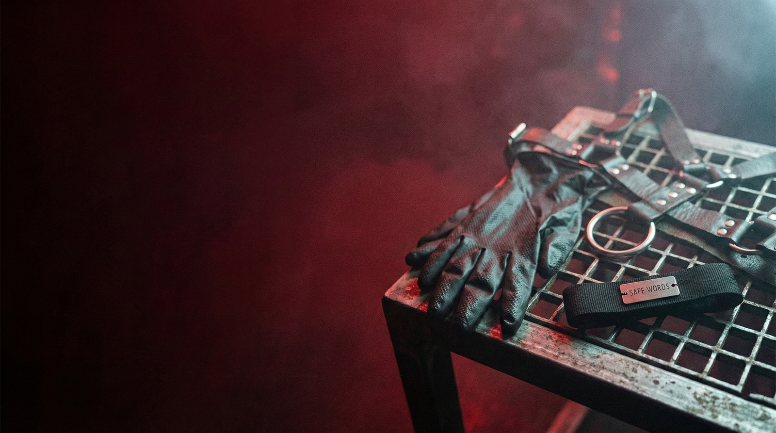 Gemini_Generated_Image_v0lp1sv0lp1sv0lp Gants noirs, harnais et bracelet Safe Words sur grille métallique, lumière rouge, ambiance soirée fetish Paris